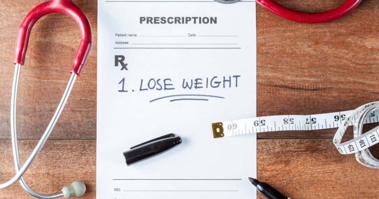 Prescription pad reading “Lose Weight” next to a stethoscope and measuring tape on a wood desk.