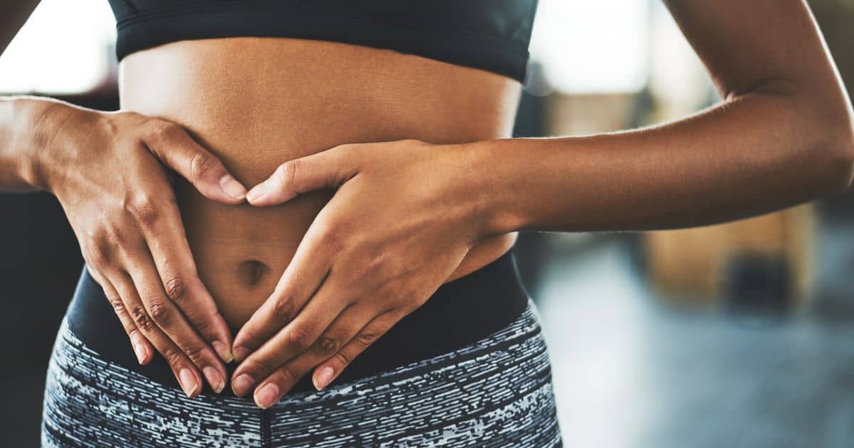 A fit woman in workout clothes forming a heart shape with her hands over her stomach, symbolizing weight loss and a healthy lifestyle.