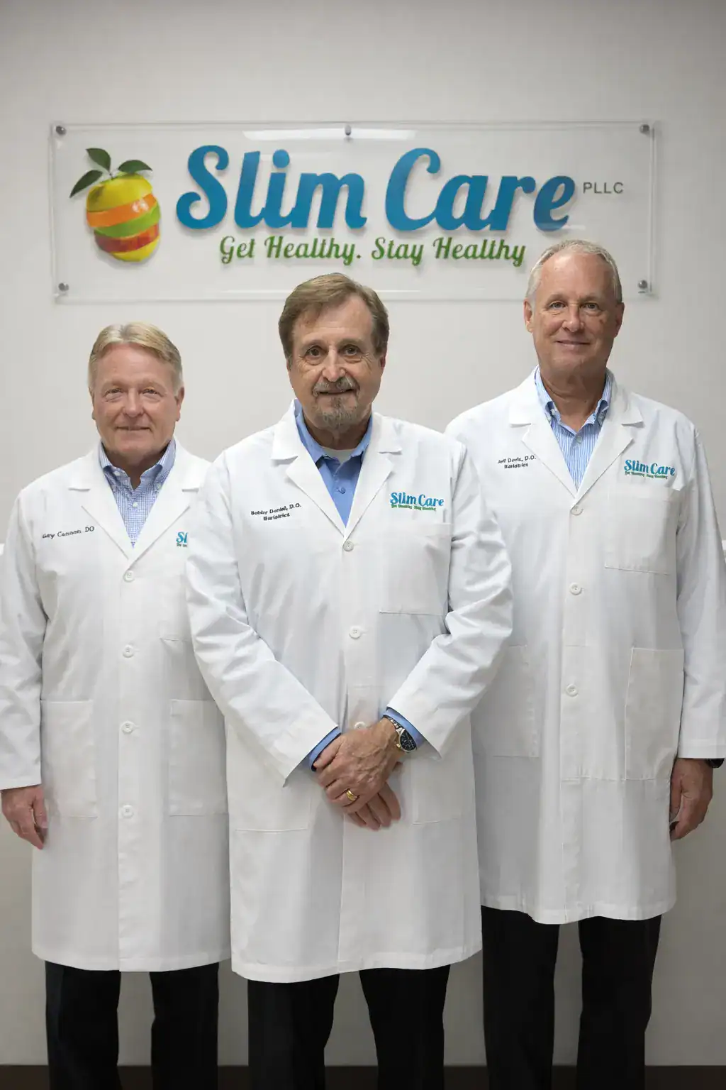 Three doctors in white coats stand together in front of a wall sign that reads “Slim Care. Get Healthy. Stay Healthy,” presenting the medical team behind the clinic. The group faces the camera in a clean clinical setting, reinforcing trust and professional care for patients.