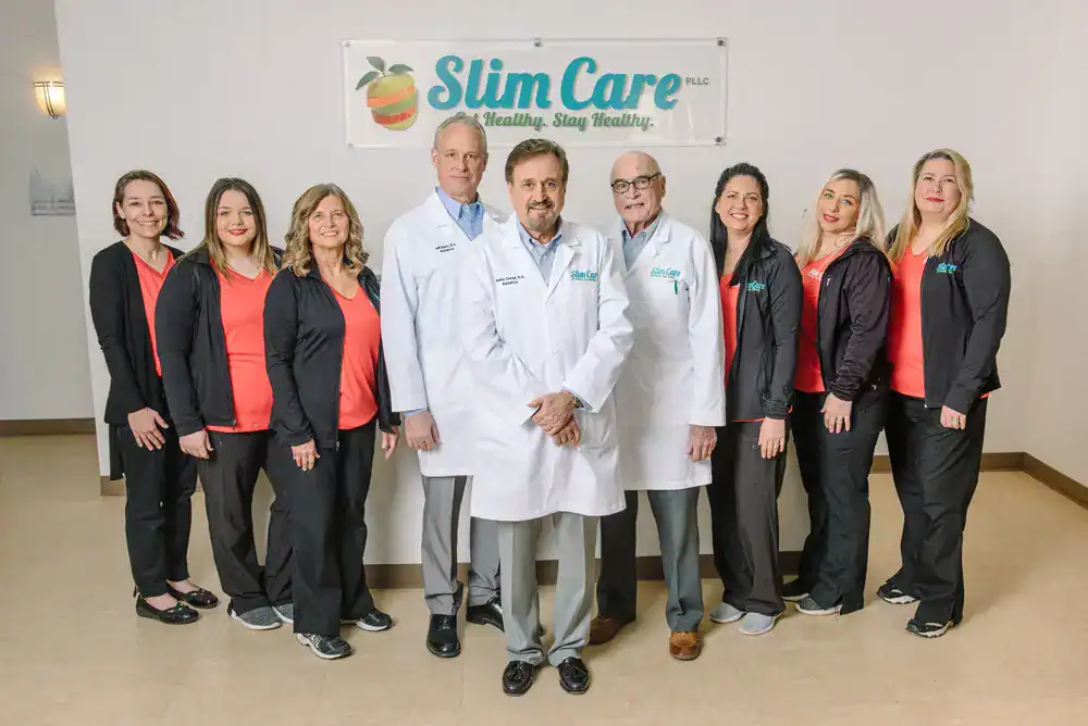 Full team of medical staff and doctors standing together under a “Slim Care. Get Healthy. Stay Healthy” sign, representing the supportive team at a weight loss clinic Tulsa patients rely on for comprehensive care.
