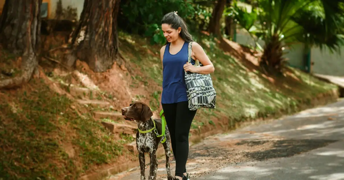 Woman in athletic clothing walking her dog along a tree-lined path outdoors.